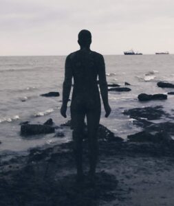 A silhouette of the statue at Margate by Antony Gormley. Two ships on horizon.