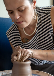 A young white woman wearing a striped t-shirt works with clay at a potter's wheel