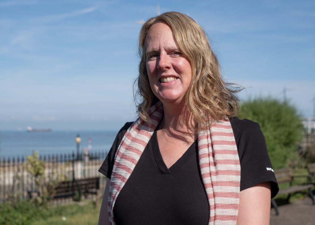 A white woman with long blonde hair wearing a black top and pink and white striped scarf