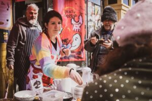 A white woman with brown hair serving food at an outside table