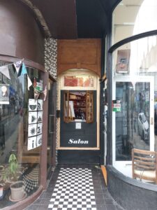 A black door with the word "Salon" written on it situated between two glass curved shop windows